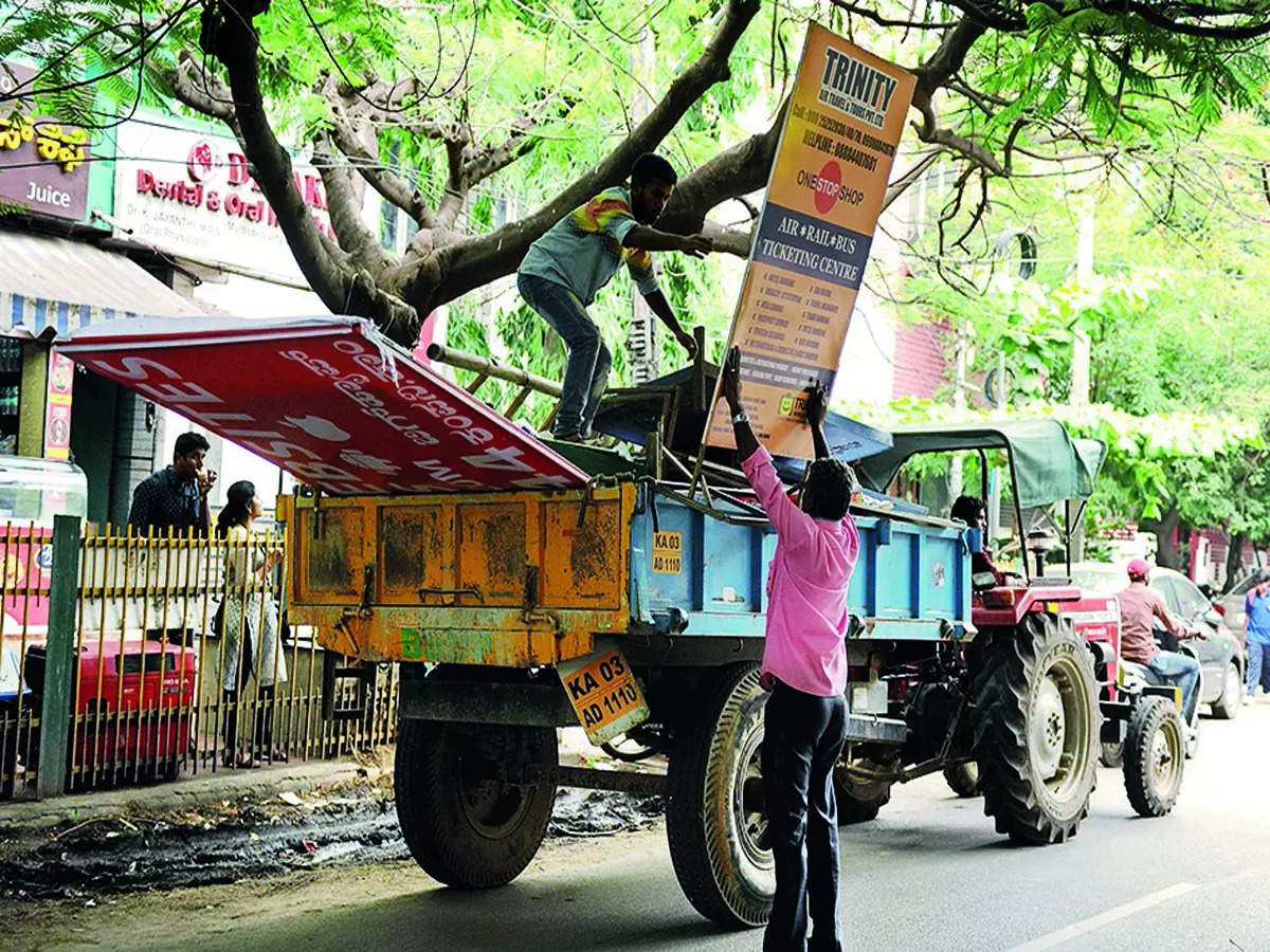 <p>File photo of BBMP workers bundling up illegal hoardings into a vehicle to dispose of them</p>