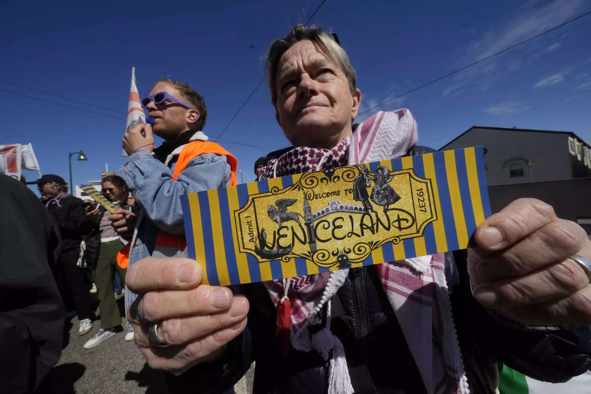 <p>A citizen shows a ticket with the writing 'Veniceland' during a protest against Venice Tax Fee in Venice, Italy, Thursday, April 25, 2024. The fragile lagoon city of Venice begins a pilot program Thursday to charge daytrippers a 5 euro entry fee that authorities hope will discourage tourists from arriving on peak days. The daytripper tax is being tested on 29 days through July, mostly weekends and holidays starting with Italy's Liberation Day holiday Thursday. Officials expect some 10,000 people will pay the fee to access the city on the first day, downloading a QR code to prove their payment, while another 70,000 will receive exceptions, for example, because they work in Venice or live in the Veneto region. (AP Photo/Luca Bruno)</p>