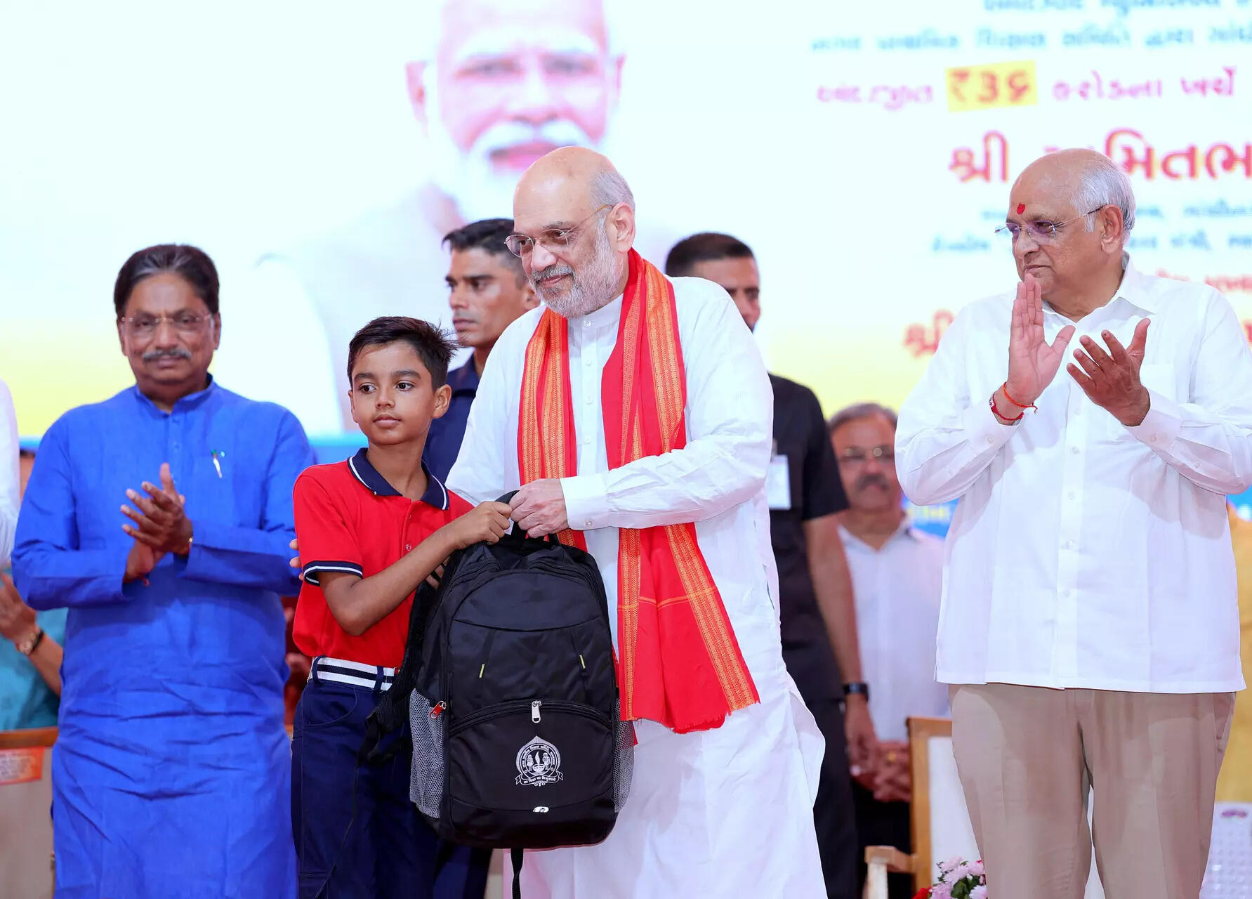 <p><strong></strong>Union Home Minister Amit Shah presents a school bag to a student during the e-inauguration of the 30 smart schools developed by AMC in Naranpura, as Gujarat Chief Minister Bhupendra Patel and others look on, in Ahmedabad on Friday. (ANI Photo)</p>