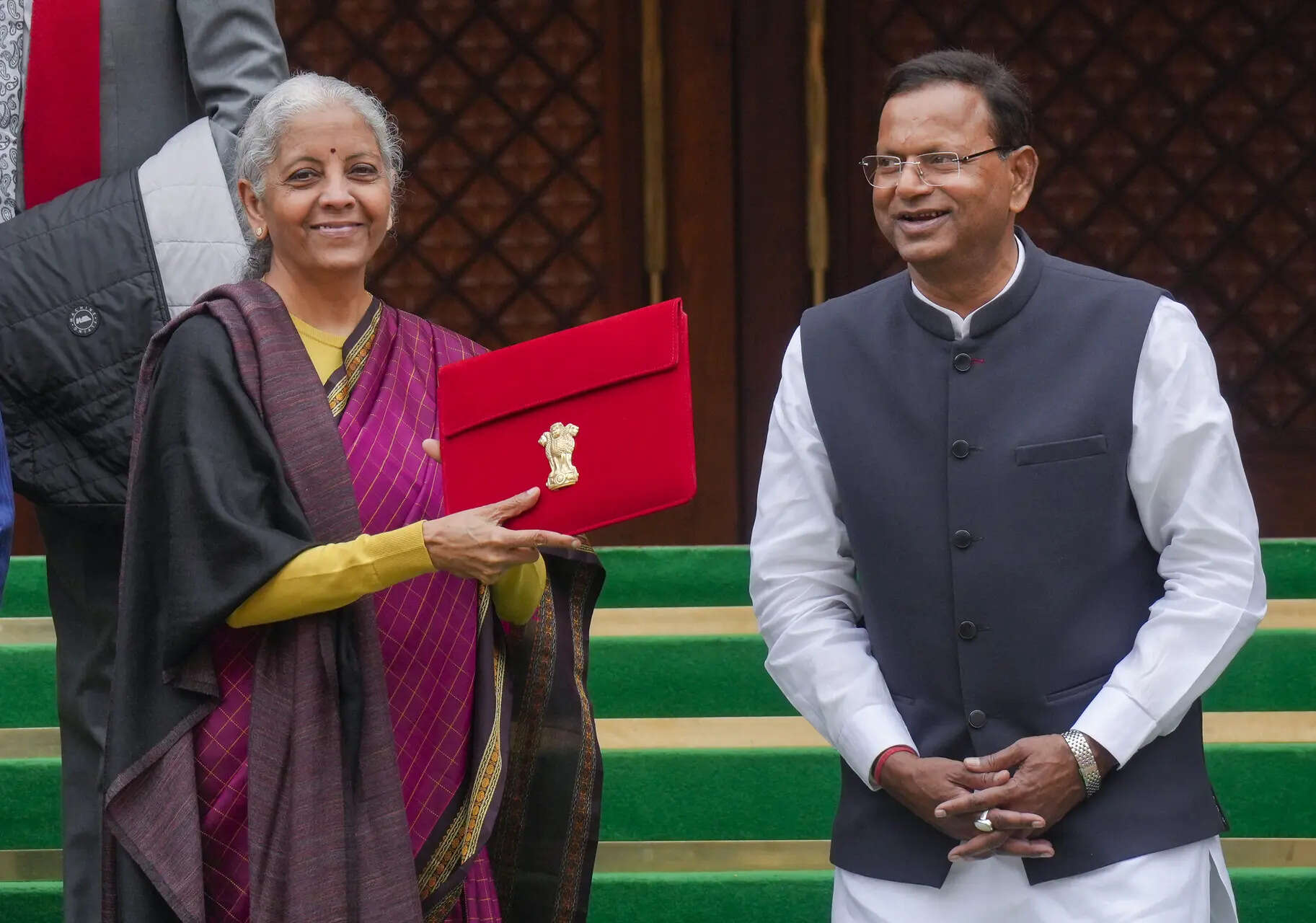 New Delhi: Finance Minister Nirmala Sitharaman shows the digital tablet, enclosed in a traditional red bahi-khata style pouch, at the Parliament premises before the presentation of the �Union Budget 2026-27�, in New Delhi. Minister of State for Finance Pankaj Chaudhary also seen. (PTI Photo/Shahbaz Khan)(PTI02_01_2026_000067A)