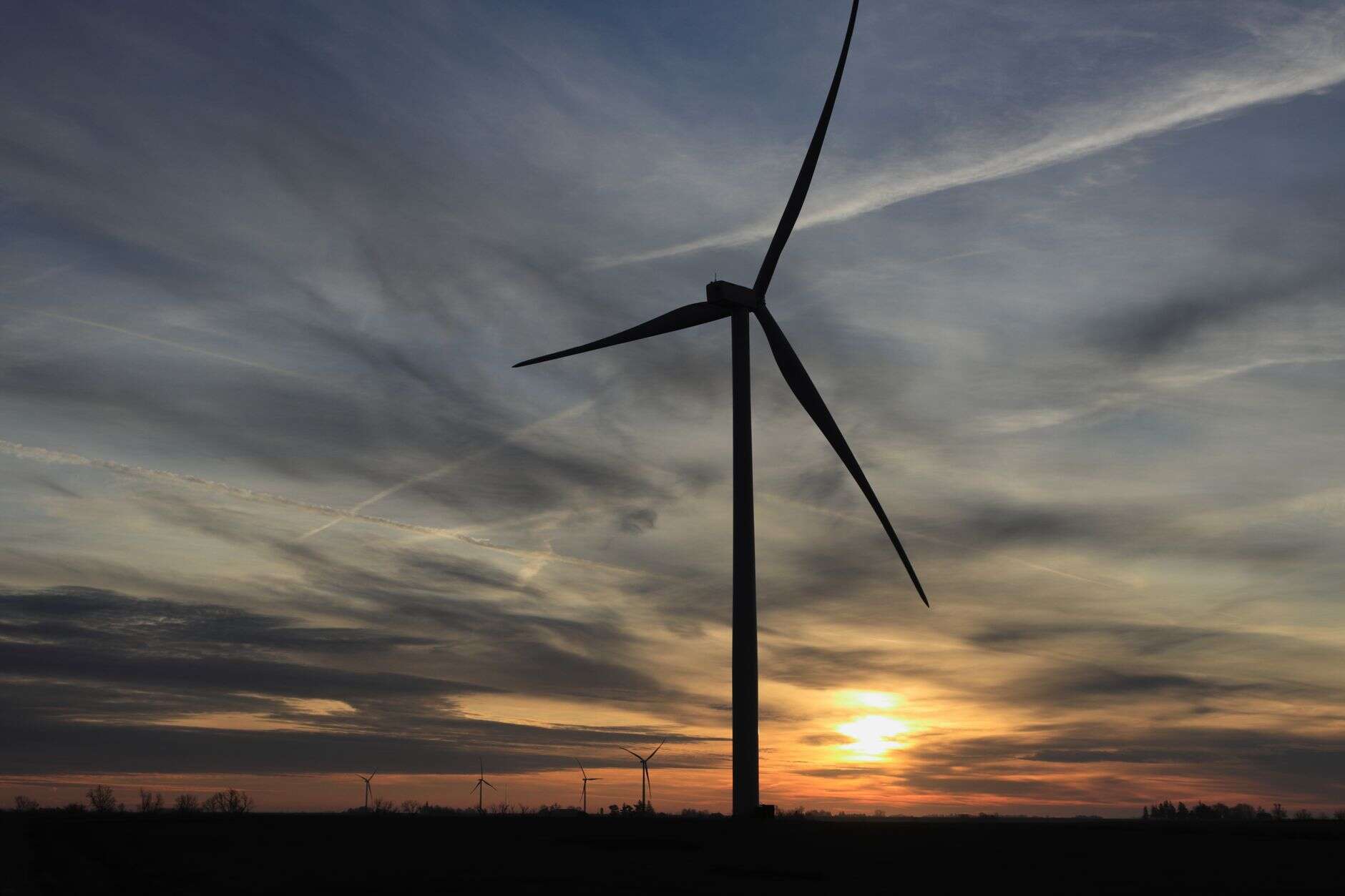 Wind turbine silhouette against a vibrant sunset, highlighting renewable energy with dramatic clouds.