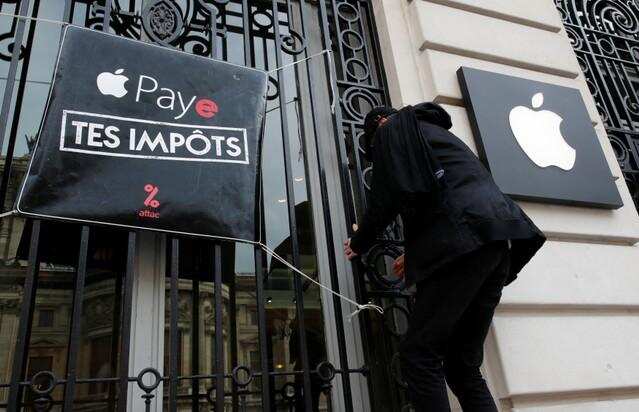 An activist from the anti-globalisation organisation, Attac, hangs a poster reading, &quot;Pay your taxes&quot;, during a protest against alleged tax evasion by Apple Inc., in front their store in Paris, France April 7, 2018. REUTERS/Philippe Wojazer