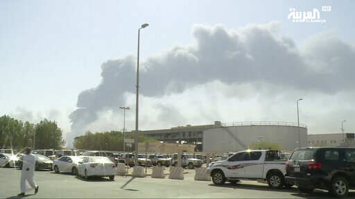 In this image made from a video broadcast on the Saudi-owned Al-Arabiya satellite news channel on Saturday, Sept. 14, 2019, a man walks through a parking lot as the smoke from a fire at the Abqaiq oil processing facility can be seen behind him in Buqyaq, Saudi Arabia. Drones launched by Yemen's Houthi rebels attacked the world's largest oil processing facility in Saudi Arabia and another major oilfield Saturday, sparking huge fires at a vulnerable chokepoint for global energy supplies. 