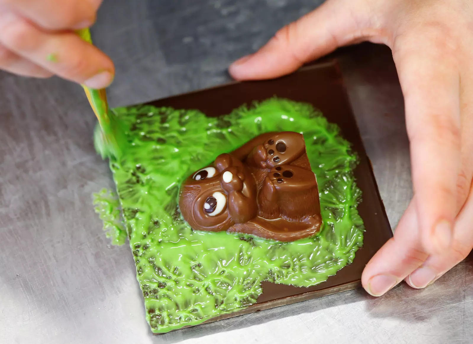 A confectioner paints green coloured liquid white chocolate around an Easter bunny during production at Eric's Confiserie Baumann in Zurich, Switzerland, March 11, 2021. (Reuters)