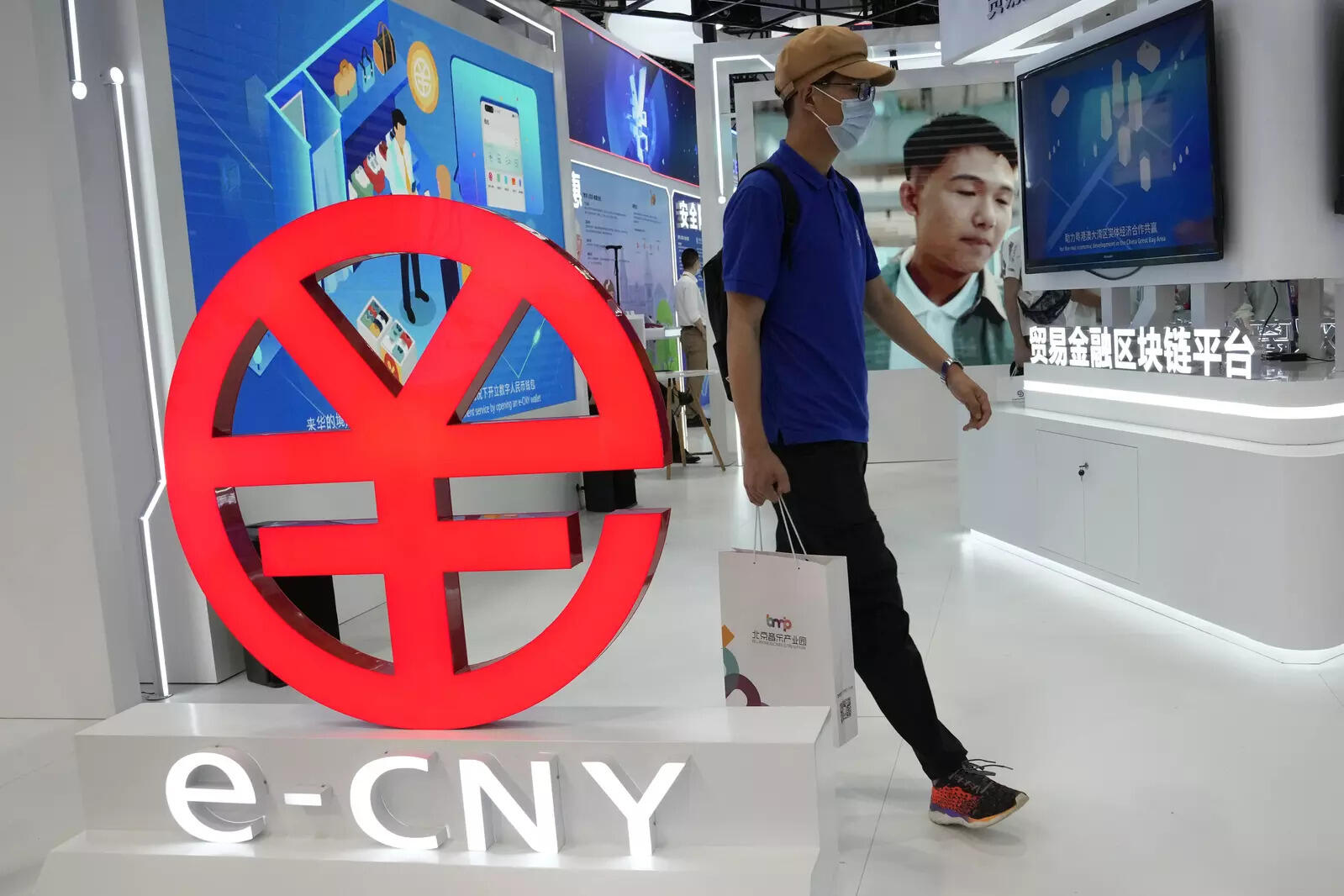 A visitor passes by a logo for the e-CNY, a digital version of the Chinese Yuan, displayed during a trade fair in Beijing, China, Sunday, Sept. 5, 2021. China's central bank on Friday, Sept. 24, 2021 declared all transactions involving Bitcoin and other virtual currencies illegal, stepping up a campaign to block use of unofficial digital money. It is developing an electronic version of the country's yuan for cashless transactions that can be tracked and controlled by Beijing. (AP Photo/Ng Han Guan)