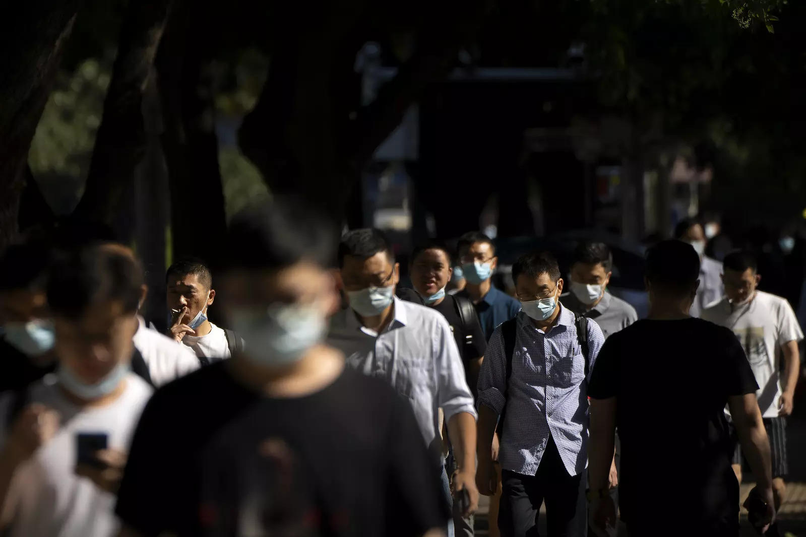   Commuters wearing face masks walk along a street in the central business district in Beijing.