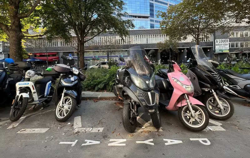 Resigned riders of gasoline-fueled motorbikes pay for parking in Paris