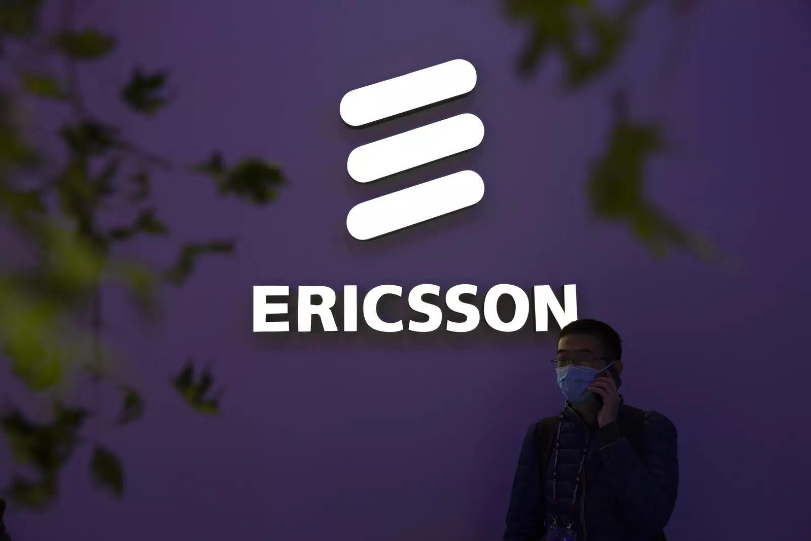 FILE - A man wearing a face mask talks on his smartphone near a booth from Swedish technology firm Ericsson at the PT Expo in Beijing, Wednesday, Oct. 14, 2020. (AP Photo/Mark Schiefelbein, File)